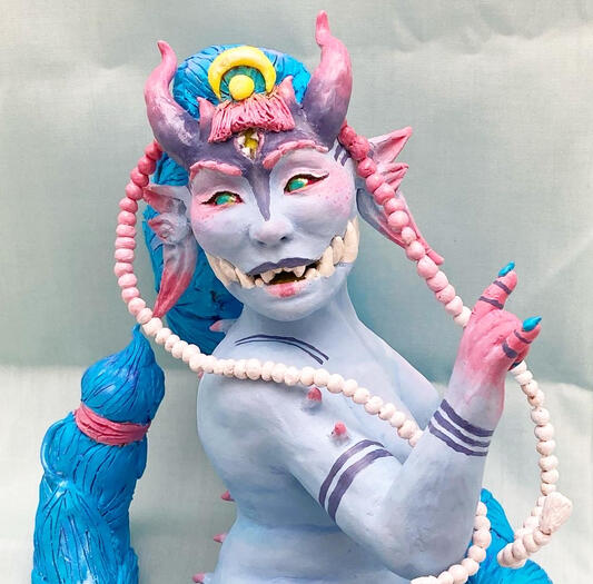 A closeup photo of a sculpture of another artist’s (Chaoillustrations) original character, Amai. She’s a blue skinned oni/demon with purple tattoos and a large toothy maw. The sculpture is made of polymer clay.